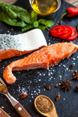 Limon, ıspanak, baharat, zeytinyağı, acı biber ve domatesli çiğ somon balığı filetosu tahtada pişmeye hazır. Ev yapımı yemek. Seçici odak 