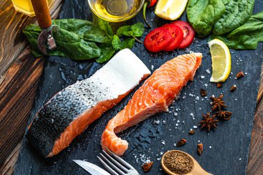 Çiğ somon balığı fileto, limon, ıspanak, baharat, zeytin yağı, kayrak kesme tahtasında pişirmeye hazır. Seçici odak 