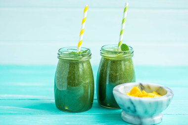 Front view of freshly blended green smoothie with mango in glass jars with straws. Turquoise blue background, copy space. Selective focus. 