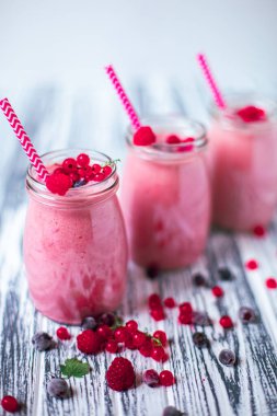 Front view of three berries milkshakes in glasses jars with straws with ingredients blueberries, raspberry, currant on wooden table. Selective focus. Healthy eating. Vegetarian diet. 