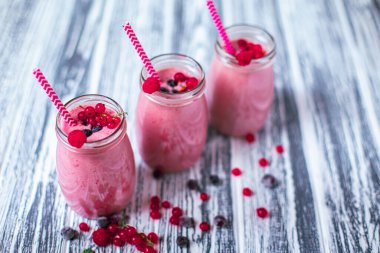 Front view of three berries milkshakes in glasses jars with straws with ingredients blueberries, raspberry, currant on wooden table. Selective focus. Healthy eating. Vegetarian diet. 