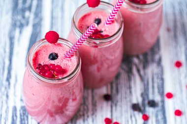 Top view of three berries milkshakes in glasses jars with straws which made from raspberry, blueberries, currant on wooden table. Selective focus. Healthy eating. Vegetarian diet. 
