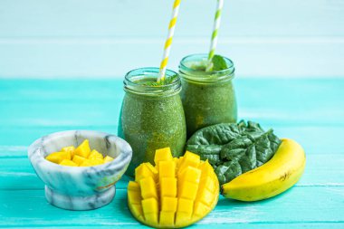 Freshly blended green smoothie with mango and banana in glass jars with straws. Turquoise blue background, copy space. Selective focus. 