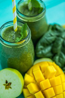 Closeup top view of freshly blended green smoothie with mango, apple, spinach in glass jars with straws. Turquoise blue wood background. Selective focus. 