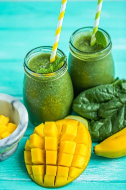 From above shot of freshly blended green smoothie with spinach, mango and banana in glass jars with straws. Turquoise blue background. Selective focus. 