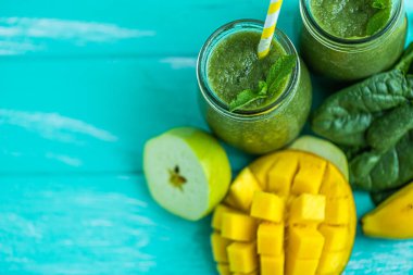 Top down view of freshly blended green smoothie with mango, apple, spinach and banana in glass jars with straws. Turquoise blue wood background, copy space. Selective focus. 