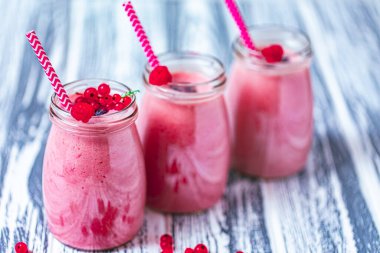 Front view of three berries milkshakes in glasses jars with straws with ingredients blueberries, raspberry, currant on wooden table. Selective focus. Healthy eating. Vegetarian diet. 