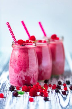 Front view of three berries milkshakes in glasses jars with straws with ingredients blueberries, raspberry, currant on wooden table. Selective focus. Healthy eating. Vegetarian diet. 