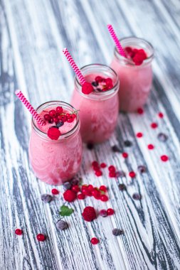 Front view of three berries milkshakes in glasses jars with straws with ingredients blueberries, raspberry, currant on wooden table. Selective focus. Healthy eating. Vegetarian diet. 