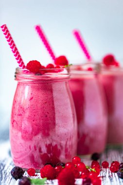 Front view of three berries milkshakes in glasses jars with straws with ingredients blueberries, raspberry, currant on wooden table. Selective focus. Healthy eating. Vegetarian diet. 