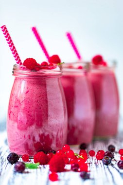 Side view of three berries milkshakes in glasses jars with straws with ingredients blueberries, raspberry, currant on wooden table. Selective focus. Healthy eating. Vegetarian diet. 