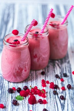 From above view of three berries milkshakes in glasses jars with straws which made from raspberry, blueberries, currant on wooden background. Selective focus. Healthy eating. Vegetarian diet. 
