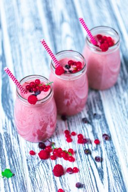 Front view of three berries milkshakes in glasses jars with straws with ingredients blueberries, raspberry, currant on wooden table. Selective focus. Healthy eating. Vegetarian diet. 