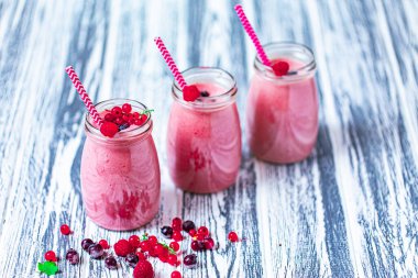 Front view of three berries milkshakes in glasses jars with straws with ingredients blueberries, raspberry, currant on wooden table. Selective focus. Healthy eating. Vegetarian diet. 