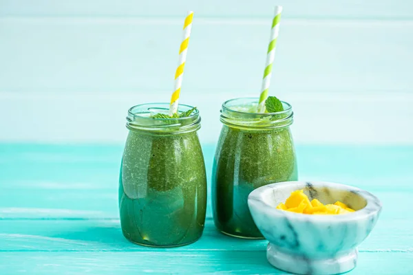 Front view of freshly blended green smoothie with mango in glass jars with straws. Turquoise blue background, copy space. Selective focus.