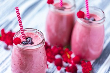 Closeup yogurt smoothie with cranberries, raspberries and blueberries standing on table in jars with straws. Fruit dessert. Berry smoothie. healthy dieting concept. Selective Focus 