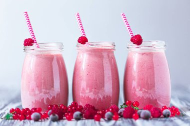 Front view of three delicious berries milkshakes in glasses jars with straws with ingredients blueberries, raspberry, currant on wooden table. Selective focus. Healthy eating. Vegetarian diet. 