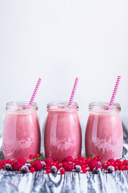 Front view of three delicious berries milkshakes in glass jars with ingredients blueberries, raspberry, currant on wooden table. Selective focus. Healthy eating. Vegetarian diet. Copy Space 