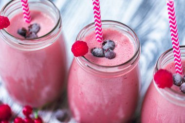 Closeup top view of three berries milkshakes in glasses jars with straws which made from raspberry, blueberries, currant on wooden background. Selective focus. Healthy eating. Vegetarian food