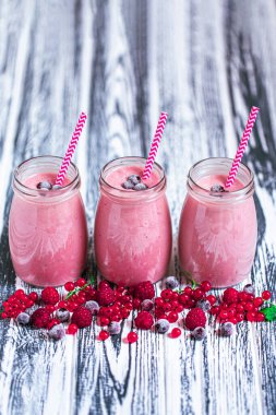 Side view of three jars of yogurt smoothie with cranberries, raspberries and blueberries standing on wooden table. Fruit dessert. Berry smoothie. healthy dieting concept. Selective Focus 