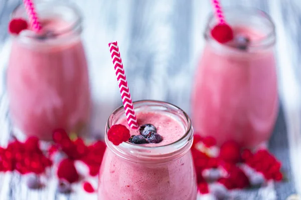 Three yogurt smoothie with cranberries, raspberries and blueberries standing on table in jars with straws. Fruit dessert. Berry smoothie. healthy dieting concept. Selective Focus