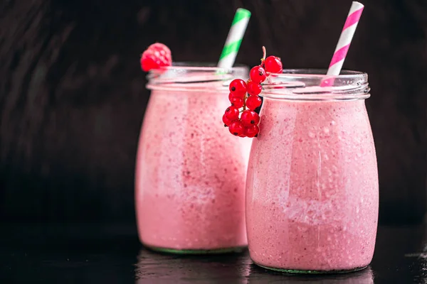 Front view of two jars of yogurt smoothie with cranberries, raspberries standing on black background. Fruit dessert. Berry smoothie. healthy dieting concept. Selective Focus