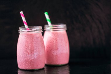 Front view of two jars of yogurt pink smoothie with berries on black background. Fruit dessert. Berry smoothie. healthy dieting concept. Selective Focus 