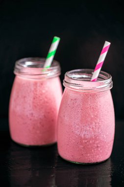 Front view of two delicious berries milkshakes in glass jars on black background. Selective focus. Healthy eating. Vegetarian diet. Selective focus 