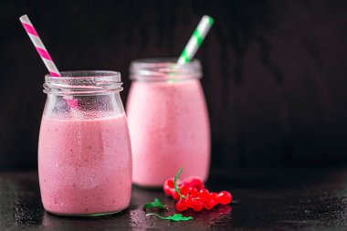 Side view of two delicious berries milkshakes in glass jars with currants on black background. Selective focus. Healthy eating. Vegetarian diet. Copy Space 