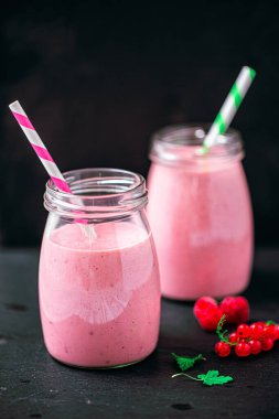 Front view of two delicious berries milkshakes in glass jars with currant and raspberry on black background. Selective focus. Healthy eating. Vegetarian diet. Selective focus 