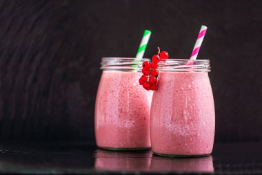 Front view of two delicious berries milkshakes in glass jars with currants on black background. Selective focus. Healthy eating. Vegetarian diet. Copy Space 