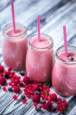 From above shot of three tasty berries milkshakes in glasses jars with straws which made from raspberry, blueberries, currant on wooden background. Selective focus. Healthy eating. Vegetarian food