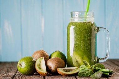 Front view of blended green smoothie in jar with fruit and vegetables on wood rustic table isolated on blue wooden background. selective focus. Healthy eating. Vitamin food 