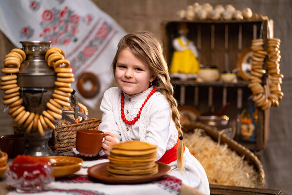 Маленькая кавказская девочка в национальном костюме, наливая чай из самовара во время празднования Масленицы. Национальные традиции.