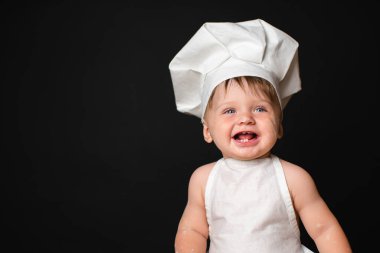 Portrait of laughing little boy in a suit of the cook dirty in flour isolated on black background. Free Space for text. Cooking concept.
