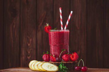 Front view of glass with fresh crimson smoothie with banana and berries on wooden table. Healthy eating concept. Vitamin food 
