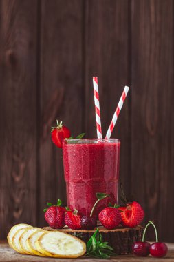 Side view of glass with fresh crimson smoothie with banana and berries on wooden table. Healthy eating concept. Vitamin food 