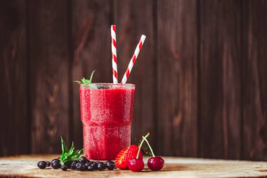 Front view of glass with fresh crimson smoothie with summer berries on wooden table. Healthy eating concept. Vitamin food. Selective focus 
