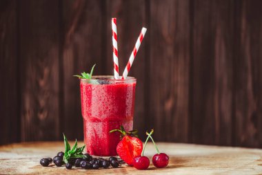Side view of glass with fresh crimson smoothie with summer berries on wooden table. Healthy eating concept. Vitamin food. Selective focus 