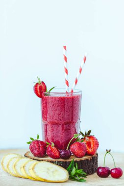 Composition of glass with fresh crimson smoothie with banana and berries isolated on blue background. Healthy eating concept. Vitamin food 
