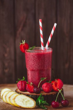 Composition of glass with fresh crimson smoothie with banana and berries on wooden table. Healthy eating concept. Vitamin food 