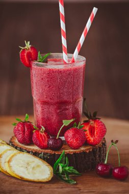 Side view of glass with fresh crimson smoothie with banana and berries on wooden table. Healthy eating concept. Vitamin food. Summer cocktail 