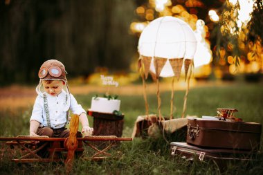 Cute little pilot boy in vintage aviator hat sitting on big toy wooden plane outdoor and playing. Happy childhood. Dream come true 