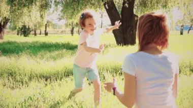 Happy little girl running on green grass in park to sitting mother, then hugging her and kissing. Slow motion. 4k