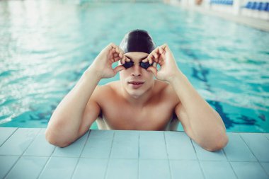 Portrait of handsome professional swimmer on edge of the swimming pool. Sport concept. Healthy lifestyle. 