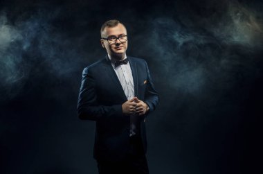 Handsome confident businessman in glasses wearing suit with bow tie standing isolated over black background while looking at camera. Space for advertising 