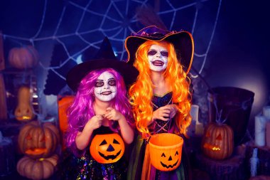 Two kid girls in witches carnival costume scaring and making faces on background decor Halloween. Trick or treating . Halloween party 