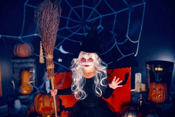Egy Kislány Boszorkány Karneváli Jelmezben Kezében Seprűvel Ijesztgetve Háttérdekoráción Halloweenkor — Stock Fotó
