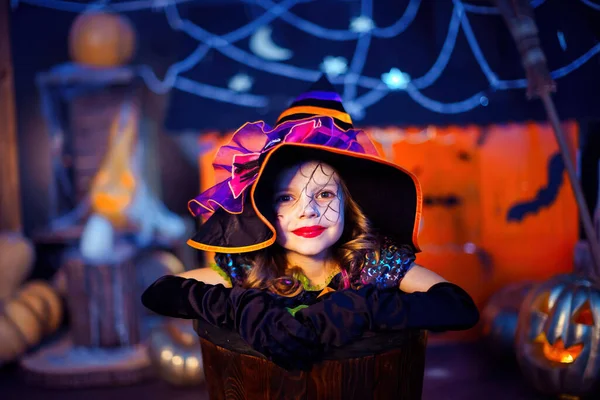 一个穿着巫婆服装的小女孩的画像从装饰之间的光晕中窥探出来 不给糖就捣蛋万圣节派对 — 图库照片