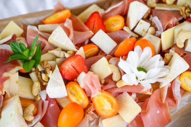 Dilimlenmiş peynirli jamon, parşömen üzerinde meyve ve bal.